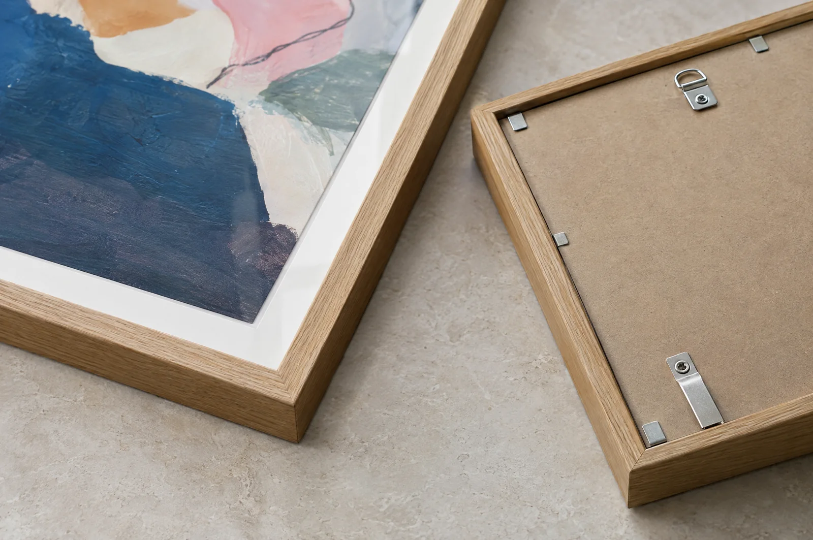 The corner of an oak frame with a white mat and acrylic glazing, and the back of a frame with security fixings